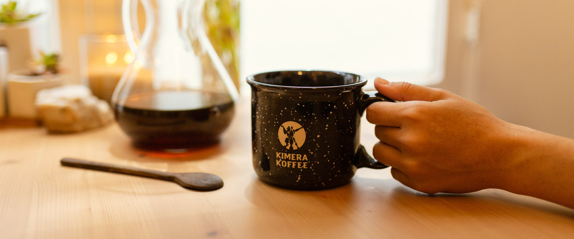 coffee mug next to chemex jar with black coffee and wooden spoon on table