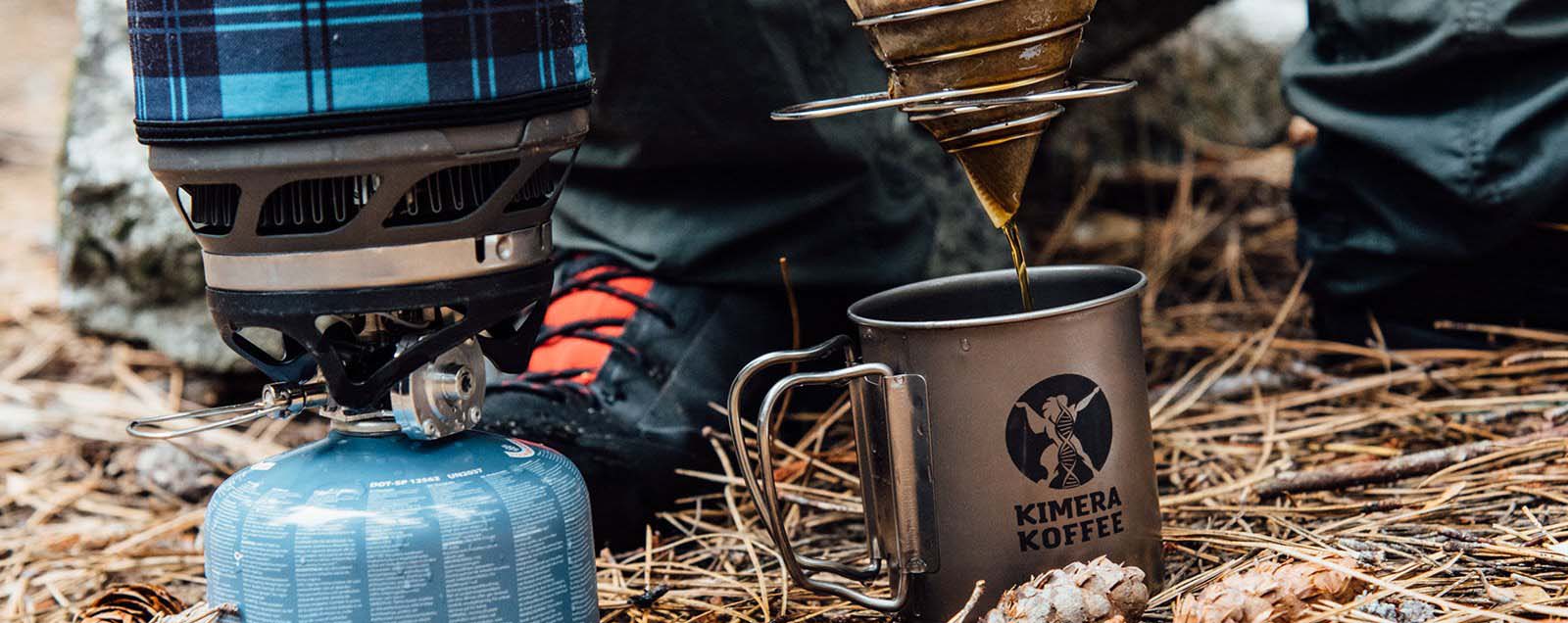 coffee being dripped into a stainless steel Kimera Koffee mug set on pine needles next to a propane camp lantern
